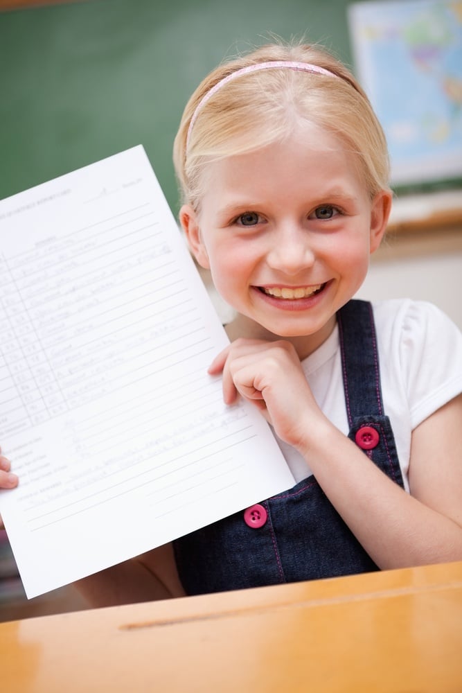 Portrait of a happy girl showing her school report in a classroom